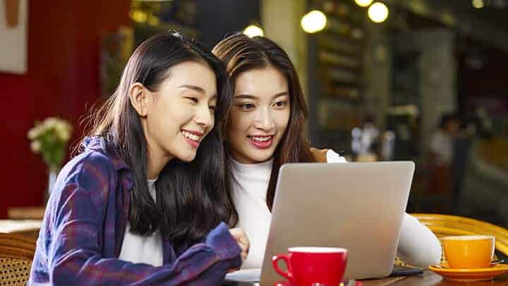 Two young asian women drinking coffee and looking at a website design on an Apple MacBook